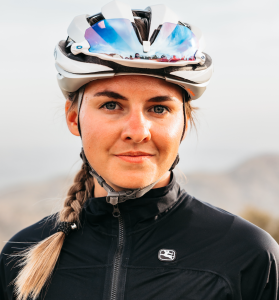 Siobhan Kelly smiling at the camera, wearing a bike helmet with sunglasses secured in it,