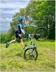 Female Mountain Bike rider performing a bike trick, standing with one foot on back tire with front tire in air