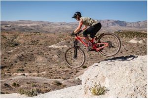 Female cyclist jumping off a rock with the desert in the background